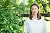 En kvinne står foran frodig grønn vegetasjon utendørs.
