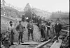 Workers stand on debris near timber supports and a hillside structure under construction or repair.