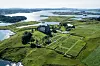 Flyfoto av Avaldsnes kirke og kirkegård. Kirken ligger på Karmøy, omringet av grønne enger og fjorden.