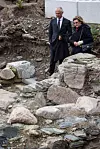 Dagfinn Skre og dronning Sonja inspiserer utgravingen av kongsgården. De går blant steinene som utgjør restene av muren til det en gang enorme bygget.