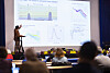 En person holder en presentasjon med flere grafer og diagrammer på en stor skjerm i et auditorium.