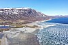 Dronefoto av innsjøen Tesse, med fjell i bakgrunnen. Det er is på deler av vannet, og deler av sjøbunnen er synlig.