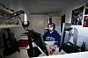 Person spiller ved et skrivebord med flere pc-skjermer i et rom med plakater og seng.