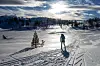 En person går på ski i et snødekt fjellandskap med spor i snøen og lav sol i bakgrunnen.