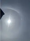 Solen lyser gjennom tynn himmel med en svak lysring rundt og en mørk bygningskant til venstre.