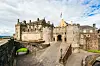 Stirling Castle i Skottland sett utenfra, med steinmurer, portrom, borggård og bro under en delvis skyet himmel.