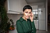 Bekymret, middelaldrende kvinne på kjøkkenet med hånden mot tinningen.