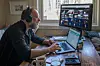Mann med hodetelefoner arbeider ved laptop og skjermer på et hjemmekontor.