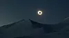 Lyset stråler fram bak en svart skive på himmelen under total solformørkelse over snødekte fjell på Svalbard under en mørk himmel.