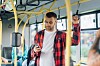 Mann i rutete skjorte ser på mobilen mens han står i kollektivtransport.
