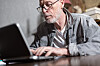 En eldre mann med briller sitter bøyd over en laptop på det som skal være et hjemmekontor.