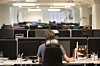 Person arbeider ved en datamaskin i et åpent kontorlandskap med flere arbeidsplasser.
