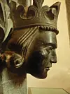 Utskåret hode i profil med dekorert krone, vist mot en lys museumsvegg.