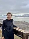 Anne Urset på en treplattform med utsikt over fjord og fjellandskap under en overskyet himmel.