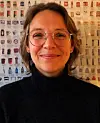 Portrett av Anna Schytte Sigaard i svart genser foran en vegg med produktbilder.