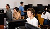 Skolegutt ved en datamaskin i et klasserom med flere elever og skjermer rundt seg.