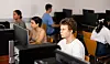 Skolegutt ved en datamaskin i et klasserom med flere elever og skjermer rundt seg.