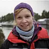 Smilende Lise Doksæter Sivle sees i i lilla lue og rød vinterjakke ved et vann.