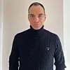 Mann i marineblå høyhalset strikkegenser fotografert mot lys bakgrunn.