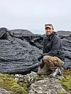 Hans Jørgen Kjøll sitter på mørke, lagdelte bergarter i et karrig fjellandskap.
