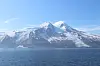 Snødekt vulkanfjell med isbreer ved en blå havoverflate under klar himmel.