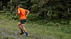 En løper i oransje skjorte jogger på en grussti i skogen.