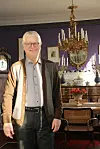 Geir Thomas Risåsen står foran en utsmykket lysekrone og antikke møbler i et historisk interiør.