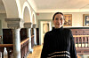 Woman in black standing inside a historic building with columns, arches and framed artwork.