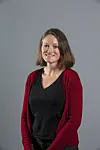 Portrett av en smilende kvinne med brunt hår, iført svart topp og rød cardigan mot en grå bakgrunn.