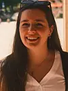 Smilende kvinne med solbriller på hodet, hvit bluse og mørk jakke.