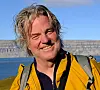 Smilende turgåer i gul jakke foran fjell og blått vann.