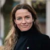 Portrett av en smilende kvinne med langt brunt hår, iført svart genser og jakke.
