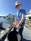 Arkeolog Leif Inge Åastveit holder i ankeret fra steinalderen. Han står på en kai med en båt til venstre. Det er sol og blå himmel og han har hatt og solbriller på.