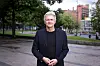 Mann i mørk jakke står i en bypark med bygninger i bakgrunnen.