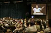 Stor forsamling ser Kåre Johan Smith tale på storskjerm i en konferansesal.