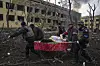 Redningsarbeidere bærer en skadet gravid kvinne på båre gjennom ruinene av et bombet sykehus i Mariupol. Vinduene er knust, røyken står ut av bygningen, og bakken er et kaos av ødelagte rester.