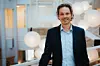 Mann i mørk dress foran glassvegger og runde lamper i et moderne universitetsmiljø.