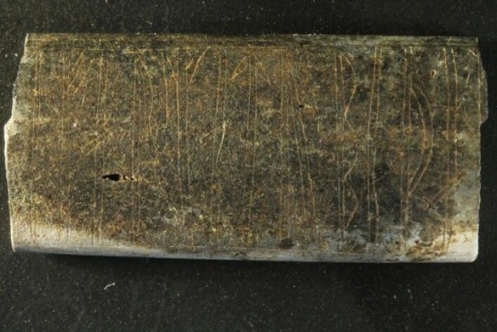 Selv etter å ha blitt børstet forsiktig, er det vanskelig å skille skrammene på den lille beinplaten, som både har blitt brent og selvfølgelig brutt ned av å ligge i jorden i over 1000 år. Platen er bare 3,8 centimeter ganger 1,8 centimeter. (Foto: Søren Sindbæk) Selv etter å ha blitt børstet forsiktig, er det vanskelig å skille skrammene på den lille beinplaten, som både har blitt brent og selvfølgelig brutt ned av å ligge i jorden i over 1000 år. Platen er bare 3,8 centimeter ganger 1,8 centimeter. (Foto: Søren Sindbæk)