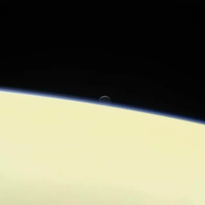 Månen Enceladus synker ned bak den store gassplaneten Saturn på dette portrettet tatt av Cassini 13. september, få dager før fartøyets endelikt. (Foto: Nasa)