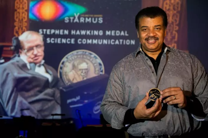 Neil deGrasse Tyson med Stephen Hawking-medaljen for forskningsformidling. I bakgrunnen på storskjerm: Stephen Hawking selv. (Foto: Max Alexander, Starmus)